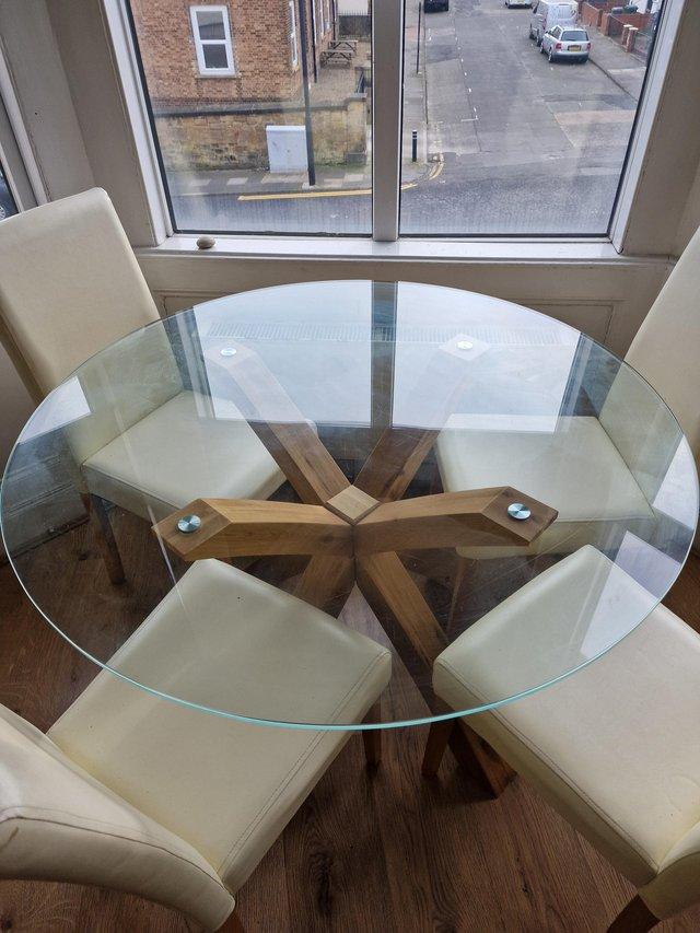 Preview of the first image of Large glass circular dining table and 4 cream leather chairs.