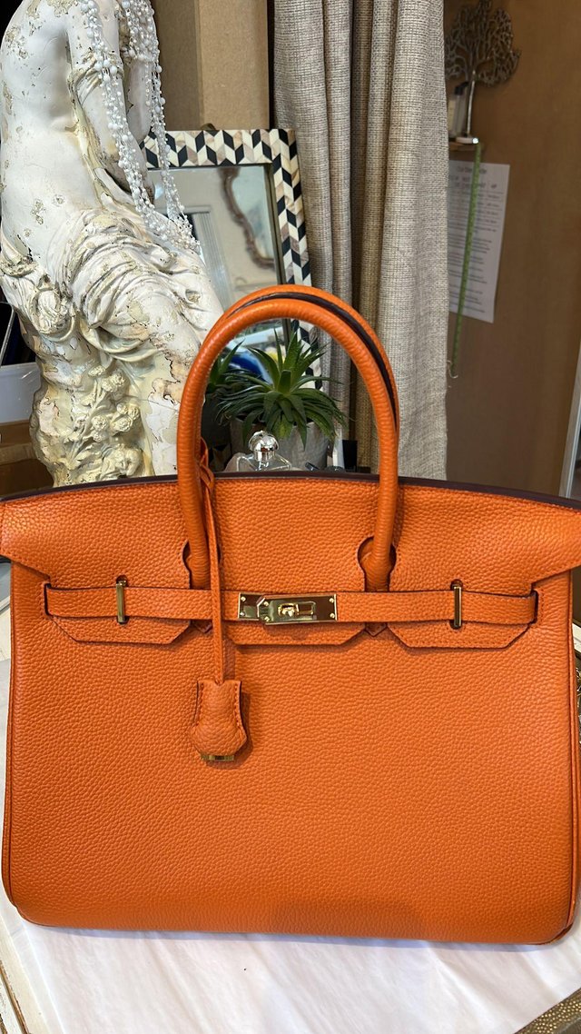 Preview of the first image of Orange leather bag with lock and dust bags.